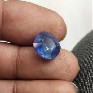 Blue gemstone held between fingers against a neutral background