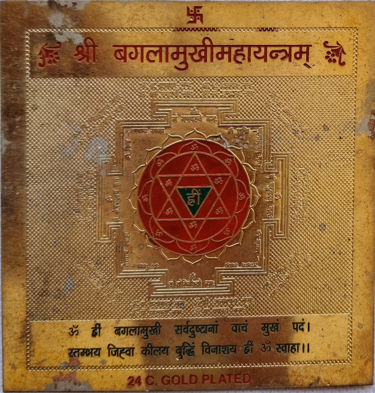 24K Gold Plated Shree Bagalamukhi Maha Yantram featuring a red central star mandala, the seed mantra Hreem, and the complete protective Baglamukhi mantra at the base.
