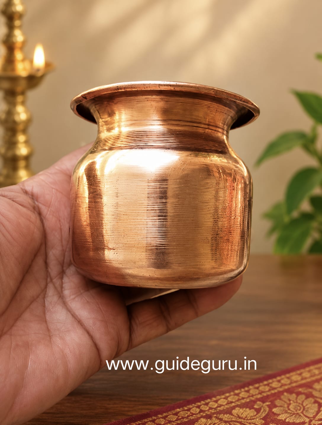 हाथ में रखा हुआ शुद्ध तांबे का चमकदार कलश या लोटा, जिसके नीचे www.guideguru.in का वॉटरमार्क है।"