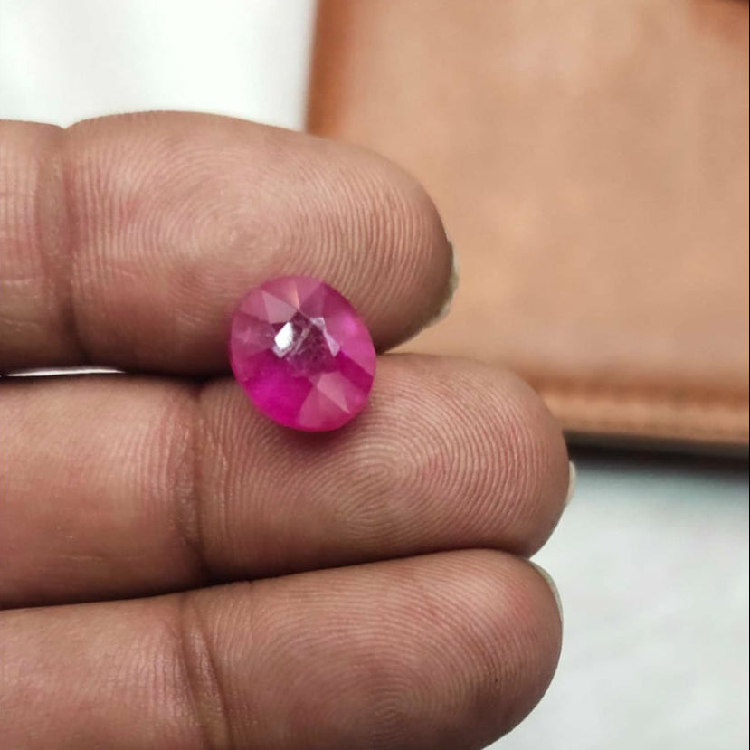 Pink gemstone held between fingers against a neutral background