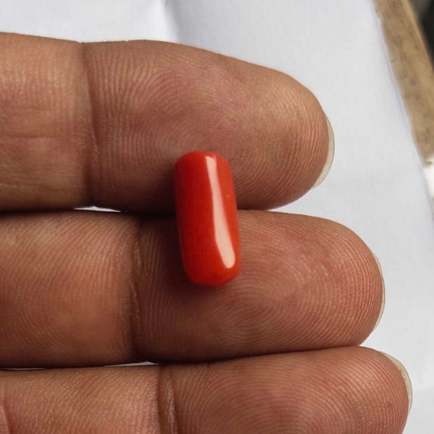 Hand holding a small red object on a white surface