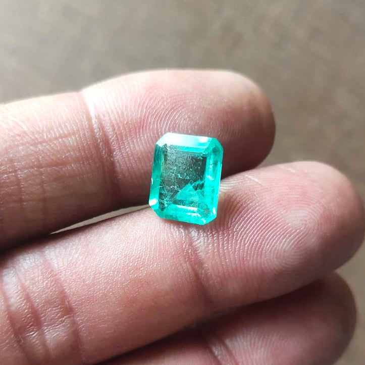 Emerald gemstone held between fingers on a neutral background