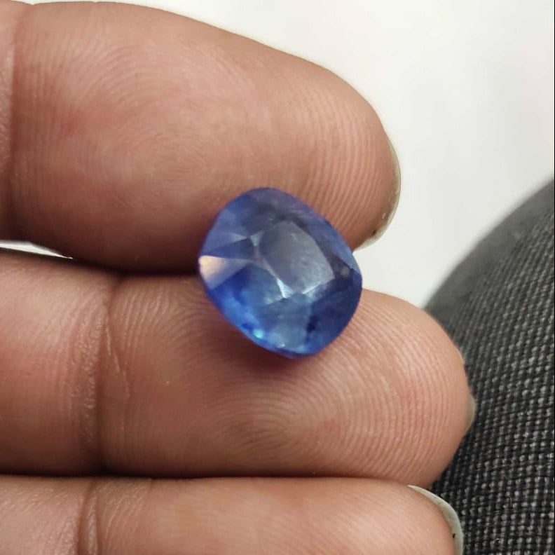 Blue gemstone held between fingers against a neutral background
